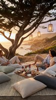 Group of diverse young adults enjoying outdoor picnic gathering under large tree with hanging lanterns at sunset by coastal cliffside location for social events and lifestyle.