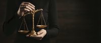 Professional lawyer holding golden scales of justice in hands against dark background symbolizing legal system fairness and judicial decision making.