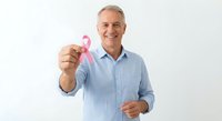 Smiling mature Caucasian man in blue shirt holding pink breast cancer awareness ribbon on white background for healthcare campaigns and medical support.