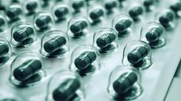 Green capsules in clear blister pack arranged in rows on pharmaceutical packaging, medical drug production background with soft focus and tonal effect.