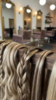 Professional hair extensions with blonde highlights displayed in modern beauty salon with styling stations and mirrors in background.