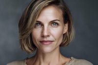 Professional blonde woman with short bob haircut smiling confidently at camera against dark background for business and lifestyle content.
