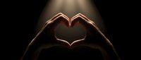 Hands forming a heart shape illuminated by a dramatic spotlight on a dark background, symbolizing love, care, and connection.