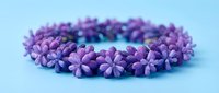Purple flower lei garland arranged in circle on light blue background for Hawaiian tropical decoration and cultural celebration events.