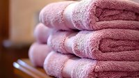 Soft pink cotton bath towels neatly folded and stacked, showing luxurious texture and plush fabric detail in warm lighting, suitable for spa and bathroom decor.