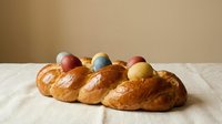 Traditional Easter bread with colorful eggs baked into golden braided dough on white cloth, festive holiday baking celebration food.