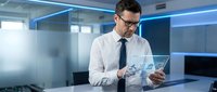 Confident Caucasian businessman in glasses using transparent tablet with financial holographic interface in modern office.