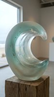 Translucent green glass wave sculpture on wooden block in modern interior space for contemporary art and home decor applications.