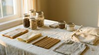 Eco-friendly zero waste kitchen essentials arranged on linen cloth near window, including glass jars with grains, bamboo straws, and reusable bags.