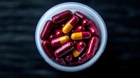 Red and yellow medical capsules and pills in white container on dark background. Pharmaceutical and healthcare concept for medicine, supplements, and drug prescriptions.