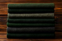 Stack of folded green and gray knitted sweaters on a wooden background, cozy autumn winter fashion concept for clothing store.