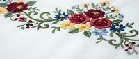 Embroidered floral design with red roses and colorful flowers on white fabric, featuring decorative swirls and leaves for textile and craft projects.