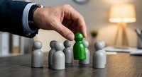 Business executive selecting green wooden figure from group of gray figures on office desk representing talent recruitment and leadership choice.