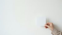 Caucasian hand holding blank white card against neutral wall background for mockup and branding purposes.