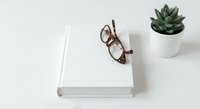 Minimalist white book with reading glasses and succulent plant on clean desk surface for modern workspace and educational content.