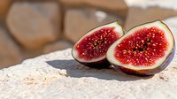 Fresh ripe fig cut in half showing vibrant red flesh and seeds on rustic stone surface in natural sunlight, macro food photography.
