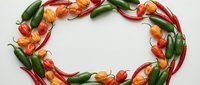Fresh red and orange chili peppers with green stems arranged in a circular frame on white background, suitable for food, cooking, and culinary design projects.
