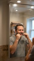 Middle-aged Caucasian man flossing teeth in modern bathroom mirror reflection showing daily oral hygiene routine and dental care habits at home.