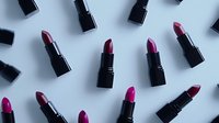 Black luxury lipsticks in various shades of pink and purple arranged in diagonal pattern on light background, creating modern minimalist makeup composition.