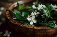 Fresh mint leaves and white jasmine flowers floating in wooden bowl with water for aromatherapy spa treatment and natural wellness rituals.