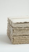 Stack of three antique handmade paper books with deckled edges and linen binding, neutral beige tones on white background.