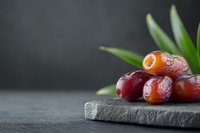 Fresh dates fruit arranged on dark slate board with green leaves creating elegant food photography composition for healthy eating and Mediterranean cuisine.