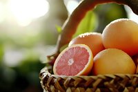 Fresh pink grapefruit and citrus fruits in rustic woven basket with soft natural lighting and bokeh background, closeup view showing juicy flesh.