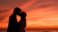 Romantic couple silhouette kissing at sunset with dramatic orange sky. Man and woman in intimate moment during golden hour for love and relationship concepts.