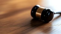 Wooden judge gavel on brown wooden table with dramatic lighting and shallow depth of field, symbolizing law, justice and legal proceedings.