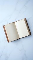 Open leather notebook with blank pages on a white marble surface, top view. Minimalist flat lay for journaling, planning, and creative concepts.