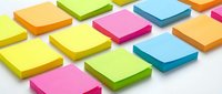 Colorful sticky notes arranged in rows on white background, featuring bright yellow, pink, green, blue and orange post-it notes for office organization and memo planning.