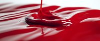 Vibrant red liquid drips and creates rippling waves on glossy surface with dramatic lighting, showing fluid dynamics in macro photography for cosmetic or food industry.