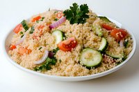 Fresh couscous salad with cucumber slices, cherry tomatoes, red onion rings and parsley garnish served on white plate, Mediterranean cuisine.