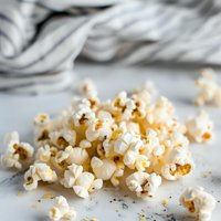 Fresh popped white popcorn scattered on light gray surface with soft textile background, macro food photography for snack and entertainment concepts.