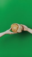 Hands passing fresh crusty artisan sourdough bread on vibrant green background. Minimalist food photography concept for bakery marketing and social media.
