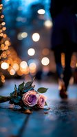Pink and purple roses lying on wet ground with romantic bokeh lights and blurred silhouette in background creating atmospheric evening mood.