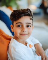 Young Middle Eastern boy in white t-shirt smiling at camera with gentle expression while relaxing on orange couch. Natural lighting creates warm atmosphere.