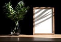 Minimal wooden frame mockup with palm leaves in glass vase on wooden surface against black wall, natural shadow overlay creates modern aesthetic.