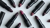 Dark purple and burgundy lipsticks scattered on white background, matte black packaging creates dramatic contrast. Professional makeup and cosmetics flatlay composition.