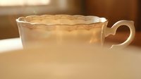 Elegant white porcelain teacup with decorative scalloped edges filled with hot beverage, steam rising in warm golden sunlight for cozy morning rituals.