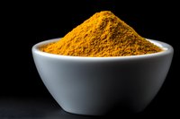 Vibrant yellow turmeric powder heaped in white ceramic bowl against black background, dramatic side lighting highlights texture and color of aromatic spice.