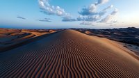 Rippled sand dunes stretch across vast desert landscape under dramatic evening sky with scattered clouds, natural patterns created by wind on golden sand slopes.