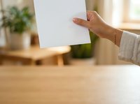 Woman holding blank white paper sheet in modern office workspace with wooden desk and green plant, suitable for mockup and branding projects.