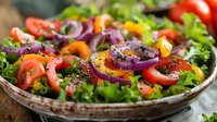 Fresh garden salad with sliced tomatoes, purple onion rings, bell peppers and mixed greens garnished with herbs and black pepper on rustic ceramic plate.