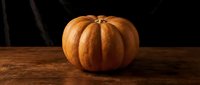 Orange pumpkin on rustic wooden table against dark background for autumn harvest decorations and seasonal cooking ingredients.