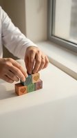 Woman hands arranging wooden blocks with wellness symbols including heart, leaf and meditation icons on white table near window for mindfulness concept.