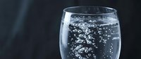 Sparkling water with rising bubbles in a clear glass on a dark background, refreshing drink concept for health and hydration.