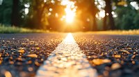 Dramatic sunset light illuminates asphalt road with bokeh effect, golden hour sun rays shine through trees creating magical atmosphere on empty path.