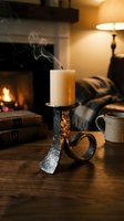 Extinguished candle with smoke rising from ornate metal candleholder on wooden table in cozy living room with fireplace and warm lighting atmosphere.