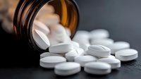 White pharmaceutical pills spilling from brown prescription bottle on dark surface, macro shot with selective focus highlighting medication and healthcare concept.